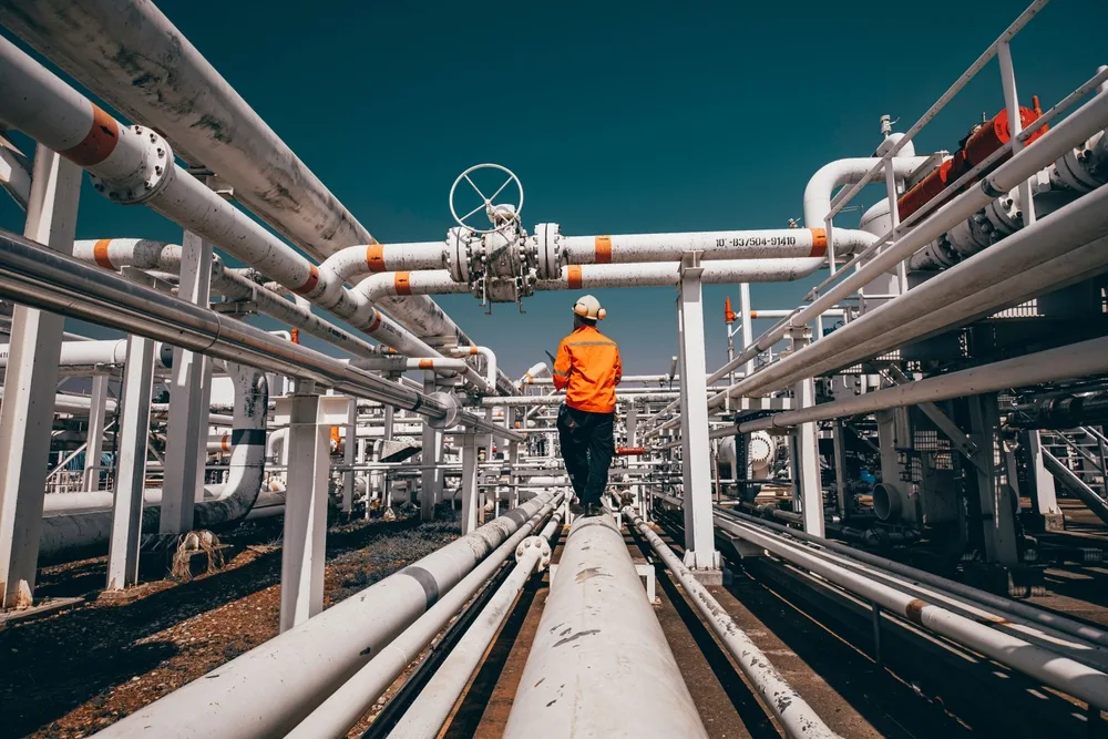 HSE adviser in long-sleeve orange PPE walking a pipe rack at a gas plant