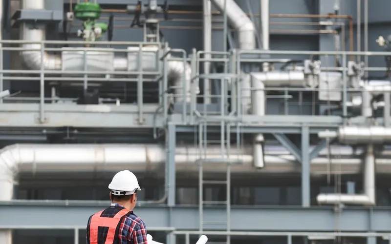 Person in a hard hat with drawings walking through a process plant